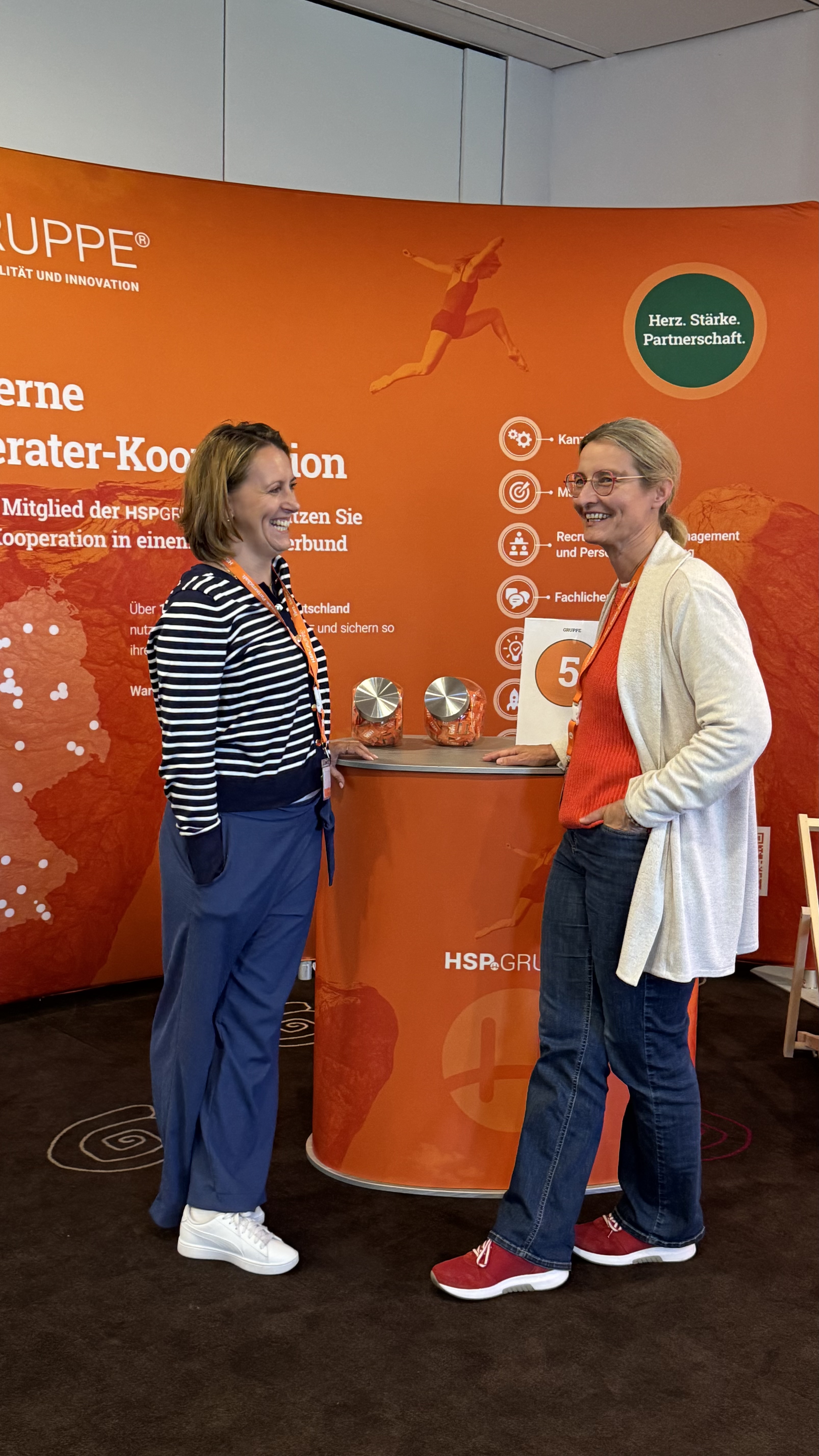 Zwei Teilnehmerinnen im Gespräch vor der orangefarbenen HSP-GRUPPE-Wand.